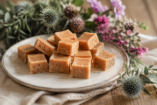 A plate of traditional Scottish tablet arranged on a ceramic plate, styled with flowers and greenery on a wooden surface.