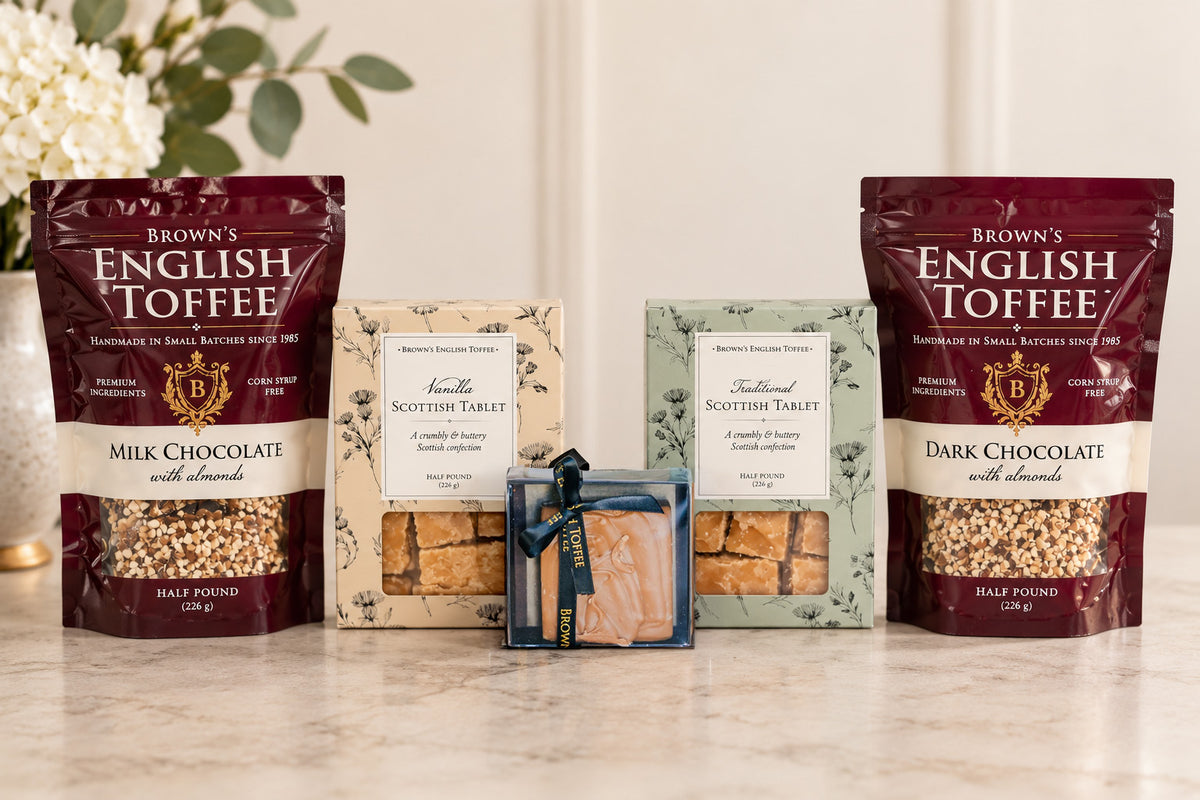 A gift assortment of Brown's English Toffee products on a marble surface, including two large bags of milk and dark chocolate toffee, two boxes of Scottish Tablet, and a small box of Honey Fudge