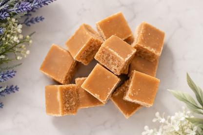 Caramel-colored scottish tablet pieces arranged on a light marble surface with decorative flowers in the corners.