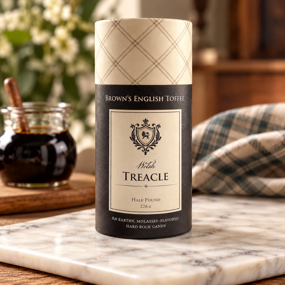 A half pound tube of Brown's English Toffee Welsh Treacle hard rock candy sits on a marble board in a warm, rustic setting with a jar of toffee and a plaid cloth in the background.